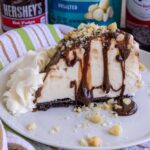 A slice of Hula Pie topped with hot fudge and chopped macadamia nuts on a white plate.