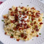 Túrós Csusza (Hungarian Cottage Cheese Noodles) topped with crispy bacon on a white plate.