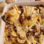 A serving spoon scooping tartiflette out of a casserole dish with gooey cheese dripping down.
