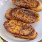 Three pieces of Spanish torrijas french toast coated in cinnamon-sugar on a white plate.
