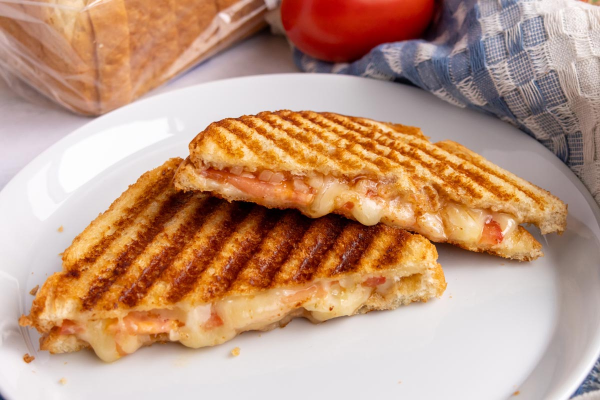 A South African Braaibroodjie sandwich with melted cheese, tomato, onion, and chutney oozing out.