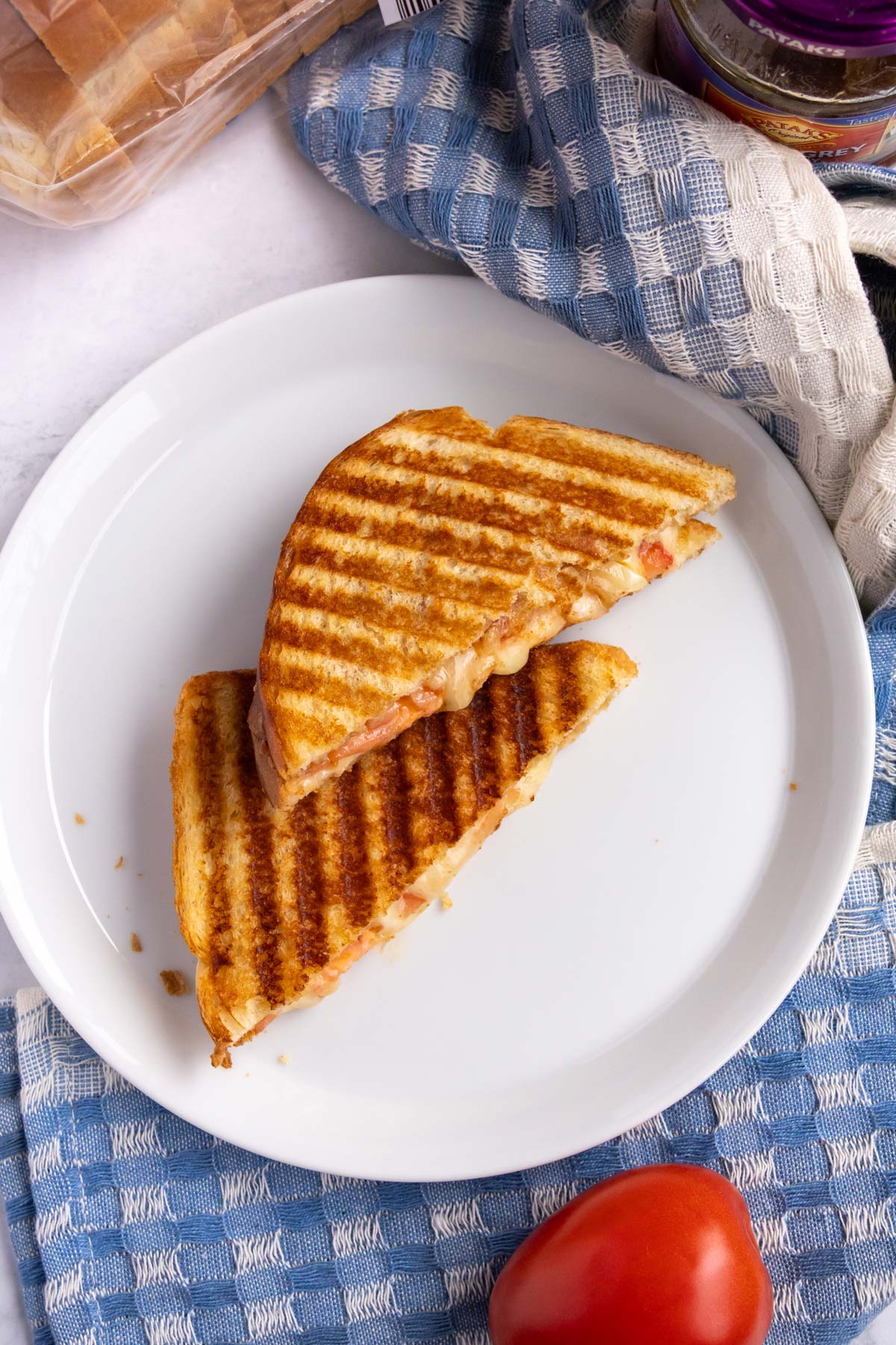 A sandwich with grill marks, cut in half on a plate over a blue kitchen towel.