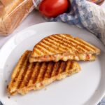 A South African Braaibroodjie sandwich cut diagonally in half on a white plate.