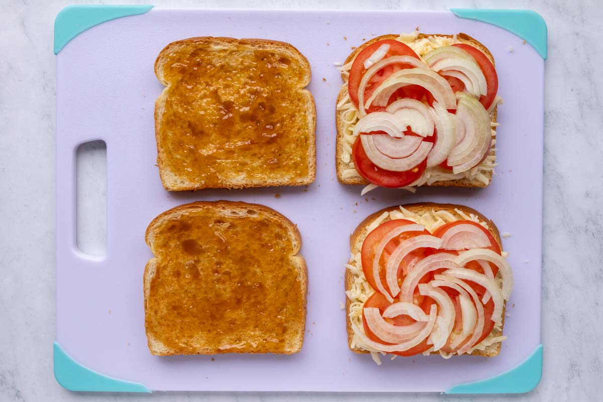 Two slices of bread topped with chutney, and two slices topped with cheese, tomato, and onion.