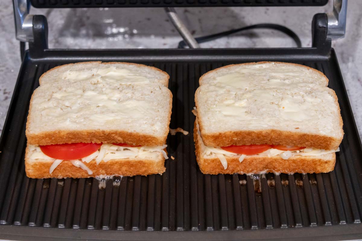 Two sandwiches coated with soft butter placed in a panini maker.
