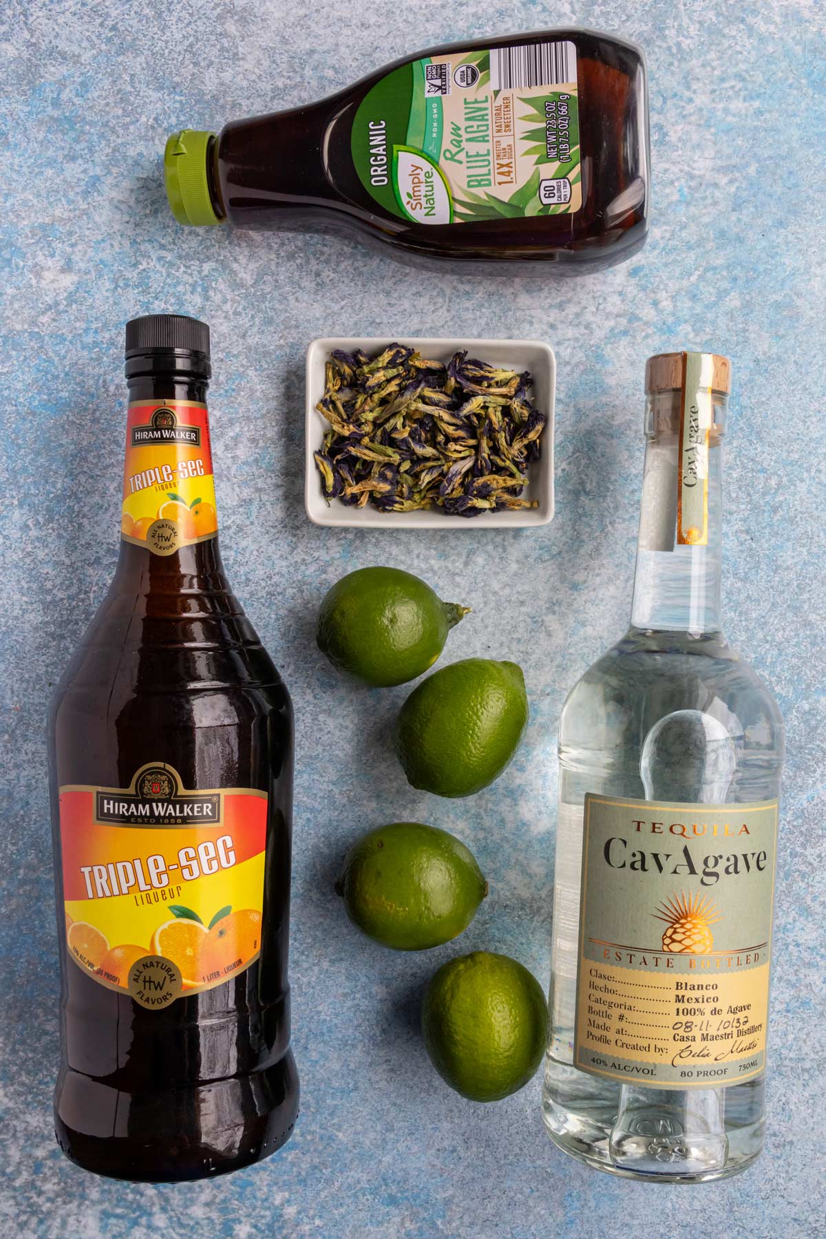 Ingredients for butterfly pea flower margaritas on a blue background.