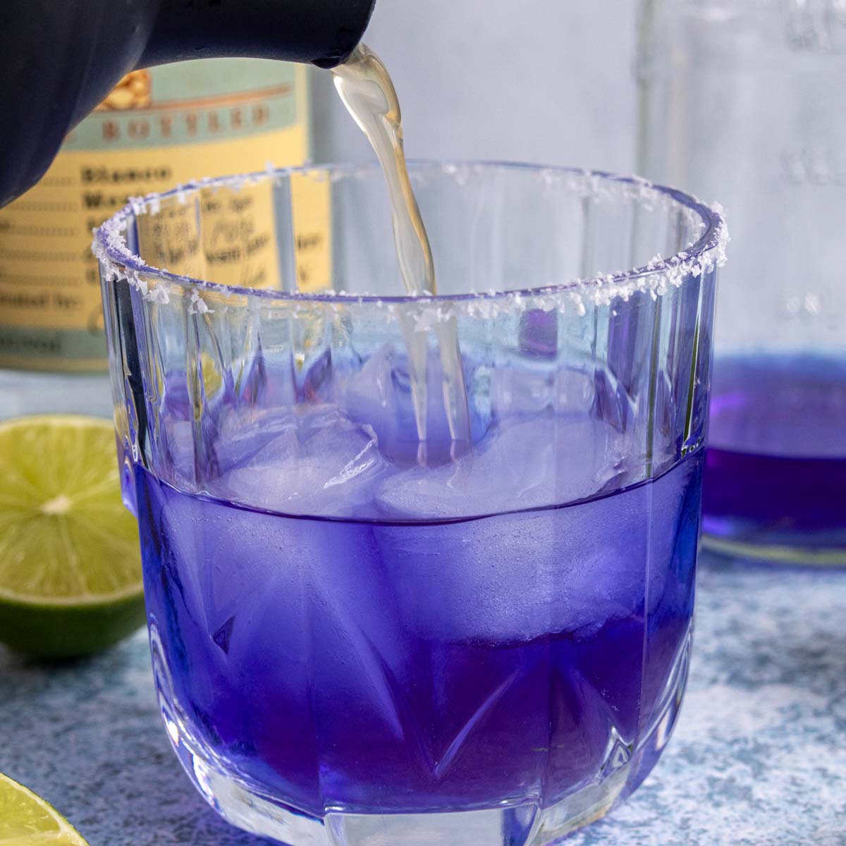 Pouring a cocktail shaker of liquid into a glass of blue tequila.