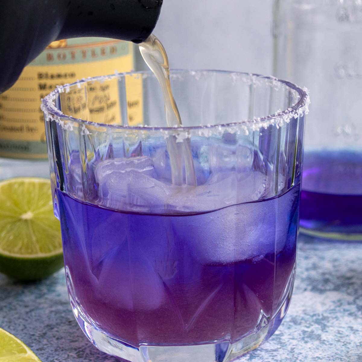 Pouring a cocktail shaker of liquid into a glass of blue tequila as it starts turning purple.
