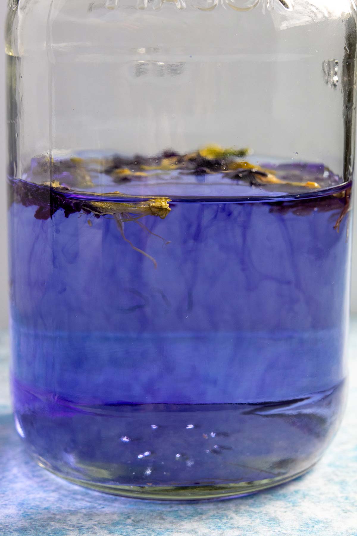 Butterfly pea flowers steeping blue color into a jar of silver tequila.