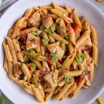 A bowl of creamy Cajun chicken pasta topped with sliced scallions.