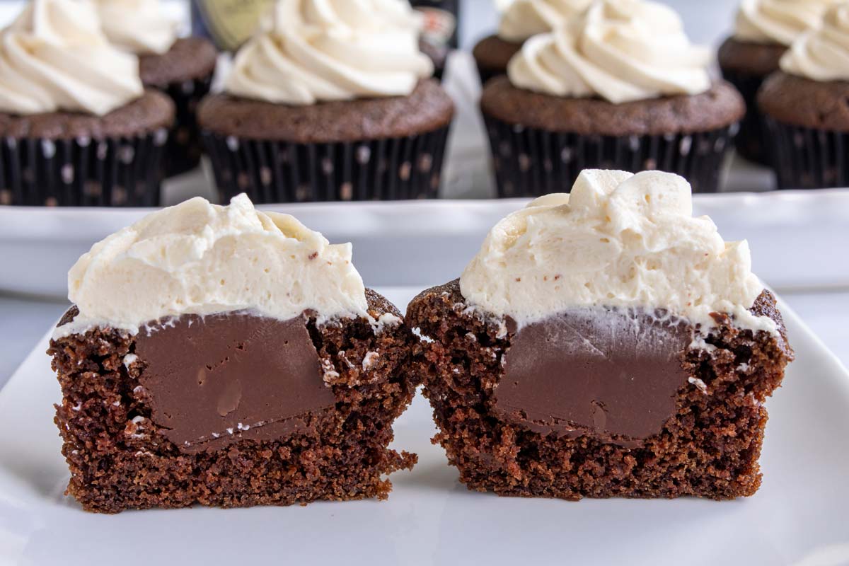 A chocolate cupcake cut in half on a white plate showing off a chocolate ganache filling.