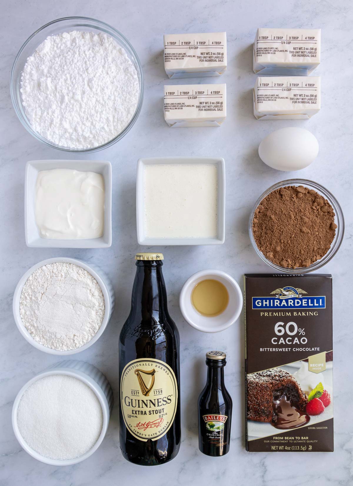 Ingredients for chocolate Guinness cupcakes with Bailey's frosting on a white marble background.