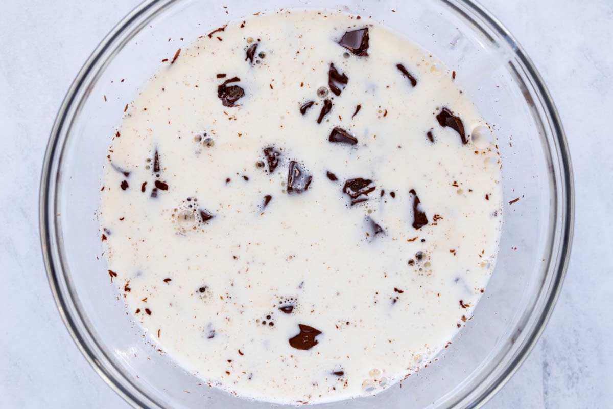 Hot heavy cream poured over chopped chocolate in a glass bowl.