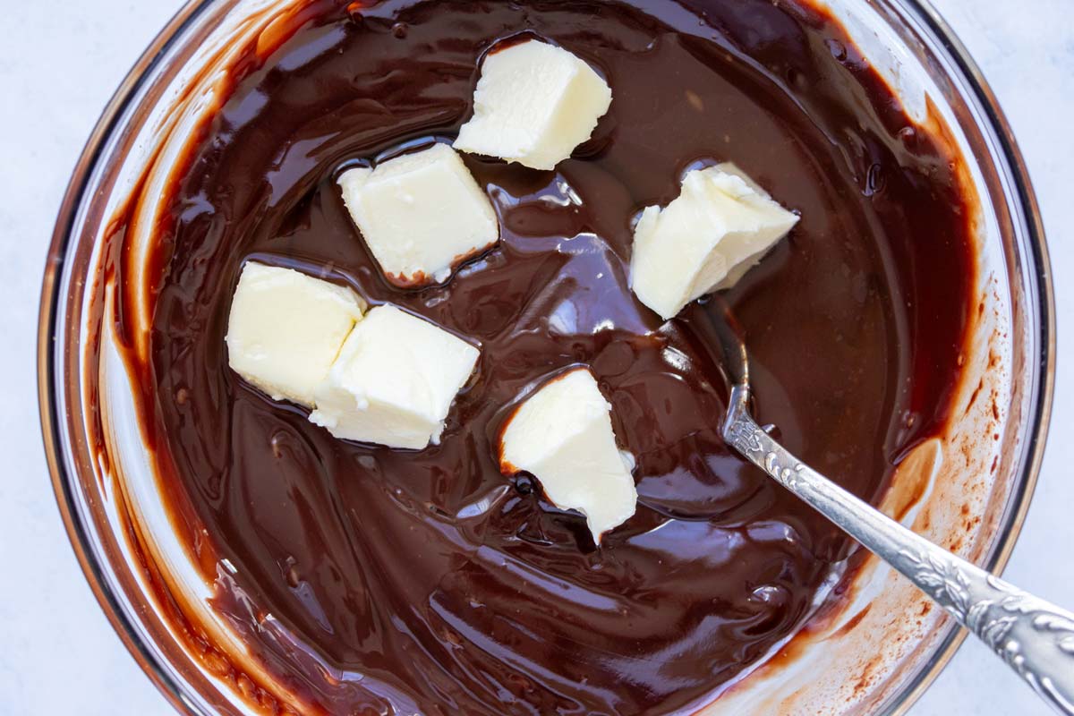 Smooth chocolate ganache in a glass bowl with cubes of butter and whiskey added to it.