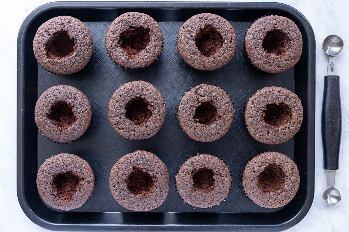 A dozen chocolate cupcakes with the centers scooped out with a melon baller.