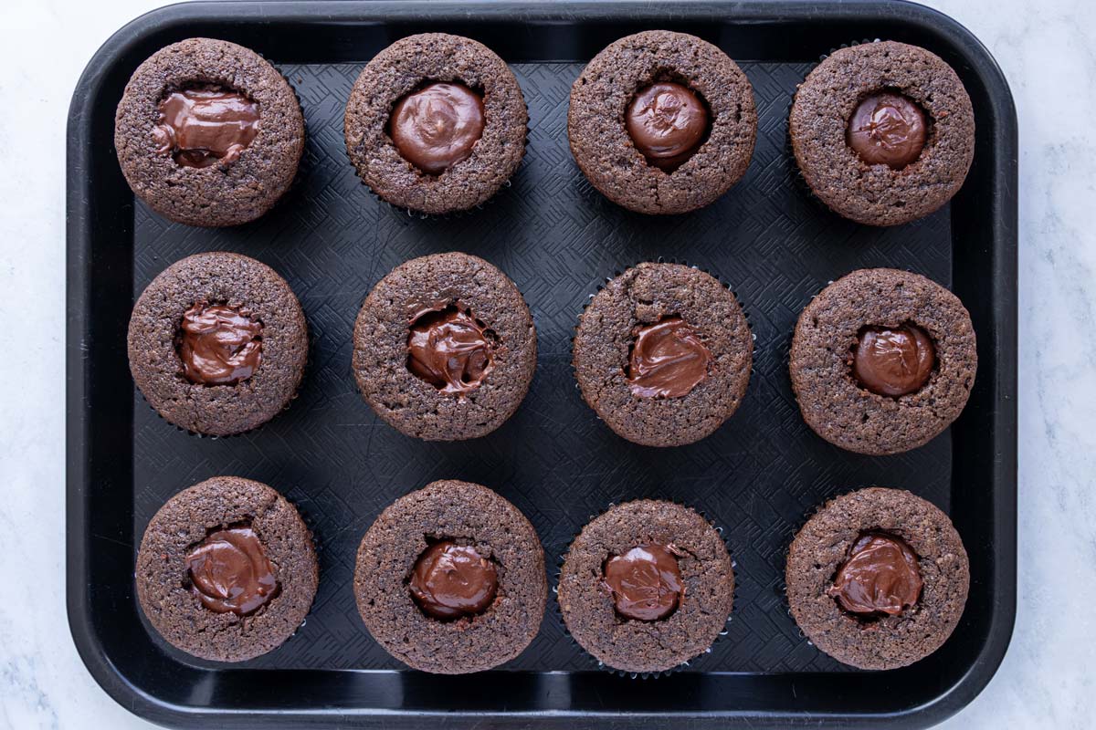 Chocolate ganache piped into the cavities in the center of a dozen chocolate cupcakes.