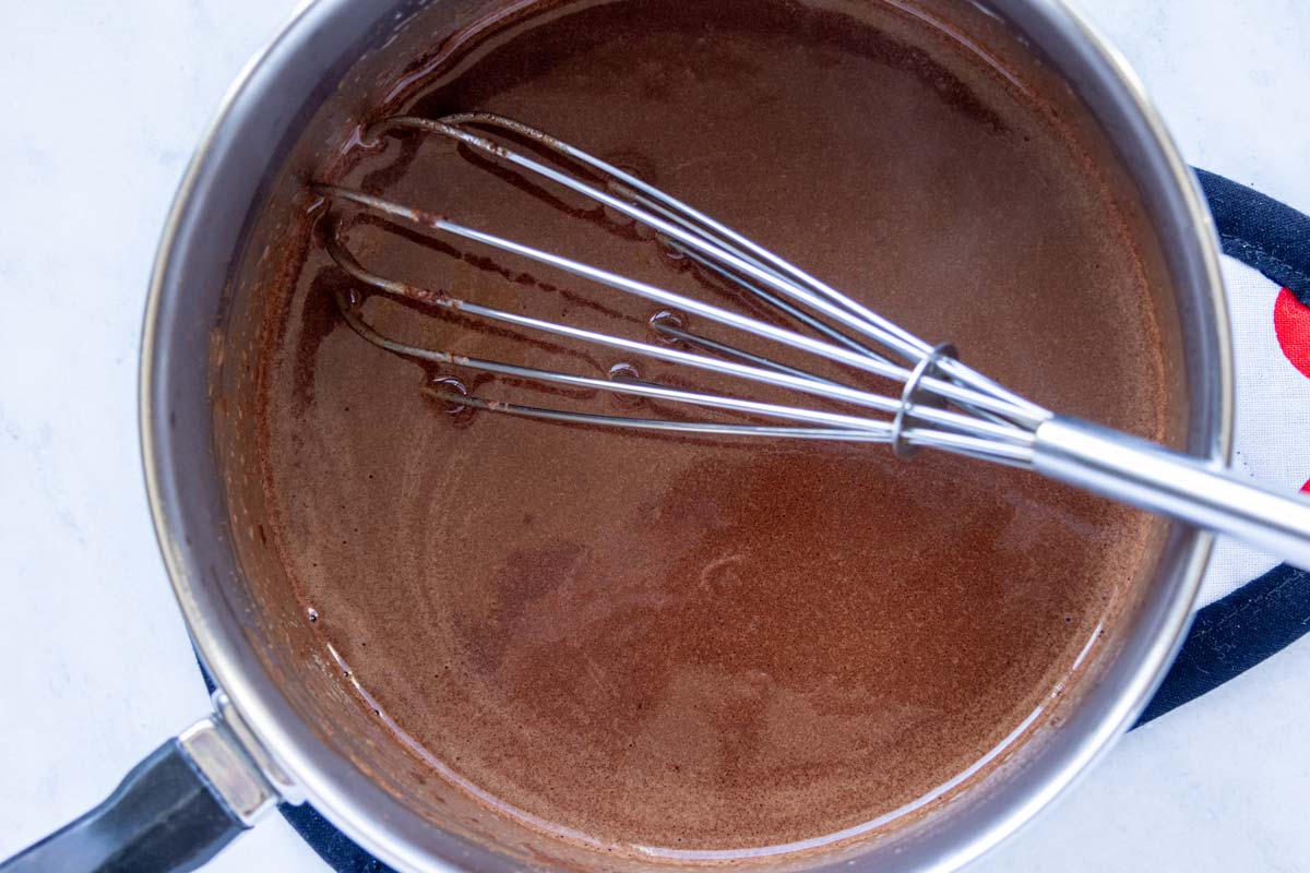 A thick chocolate liquid mixture whisked in a saucepan.