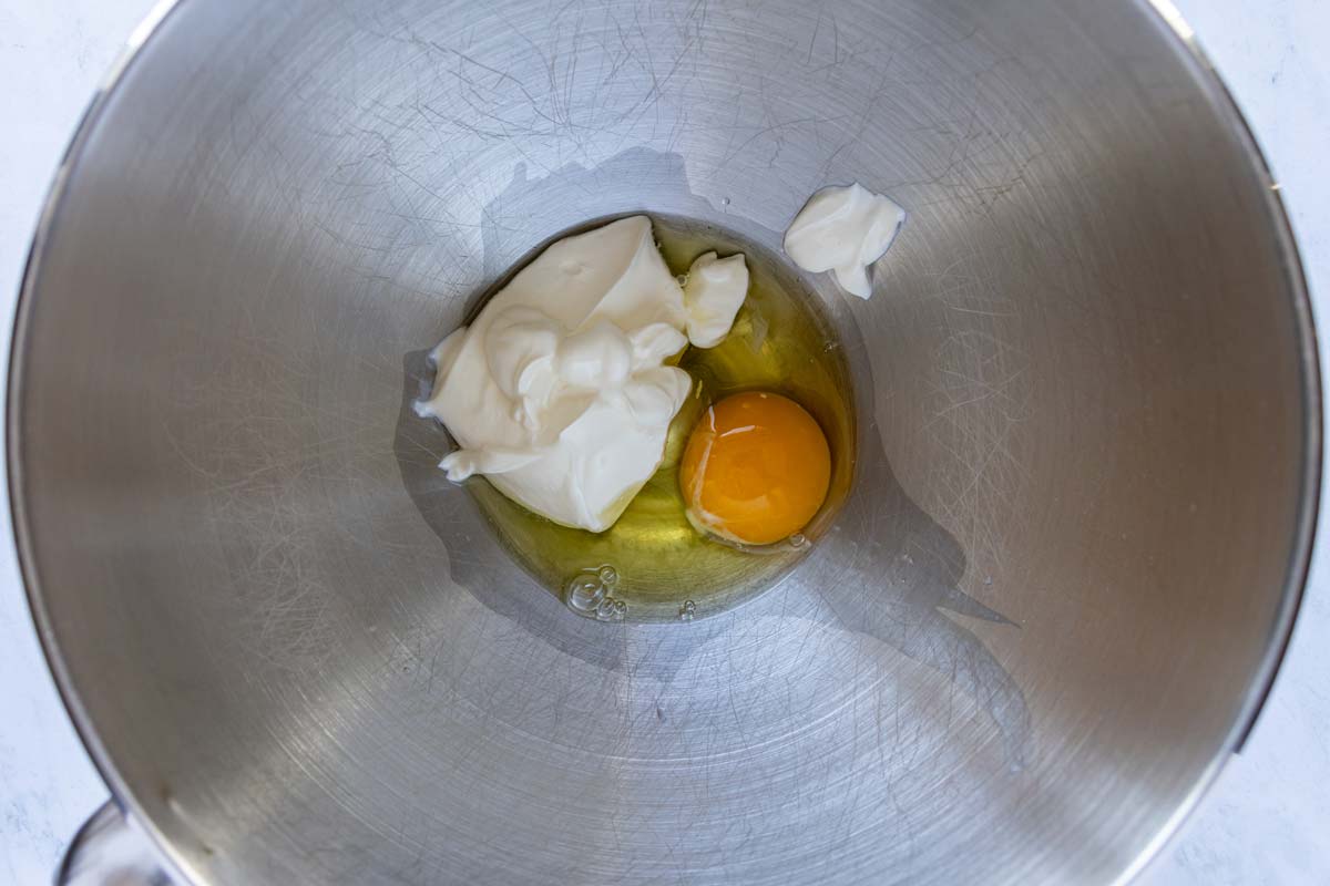 Sour cream and an egg in a metal mixing bowl.
