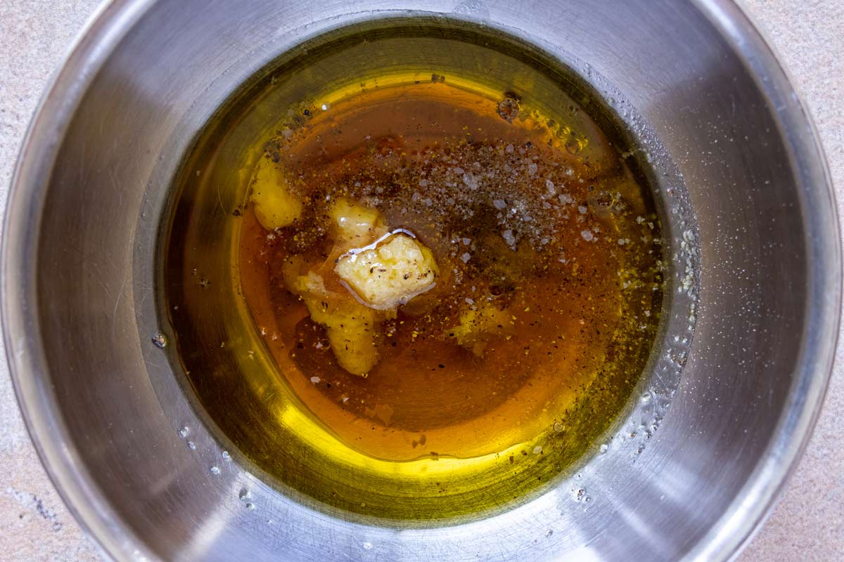 Crushed garlic, vinegar, and olive oil and seasonings in a metal mixing bowl.