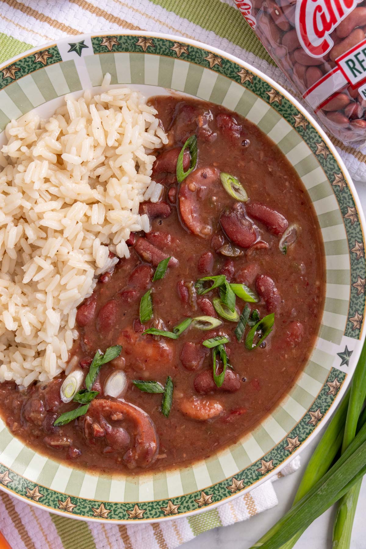 A green and white bowl filled with red beans and rice, garnished with scallions.