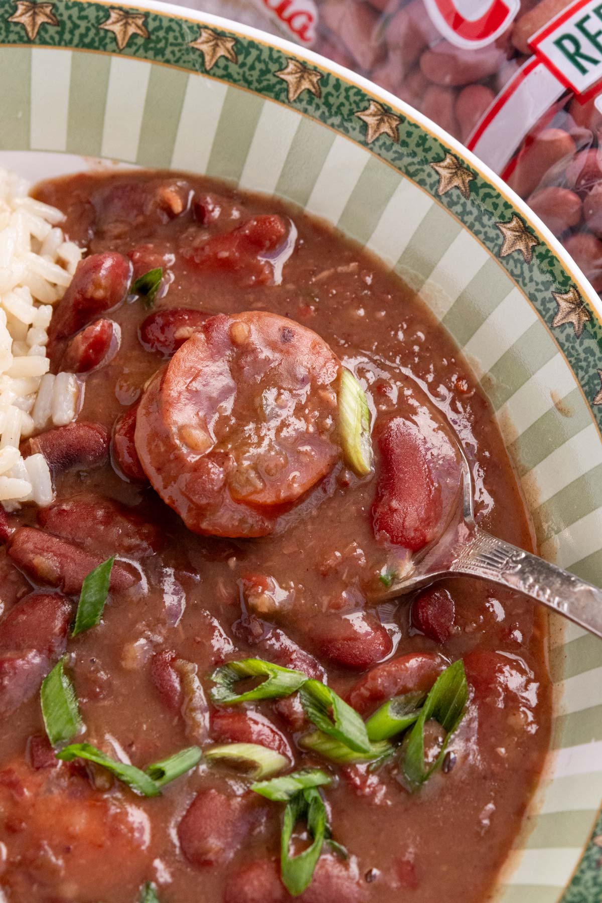 A spoon scooping some red beans and rice with andouille sausage out of a bowl.