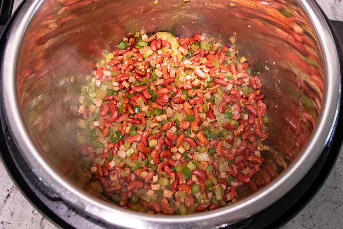 A combination of dry kidney beans and cooked vegetables and ham in an Instant Pot.