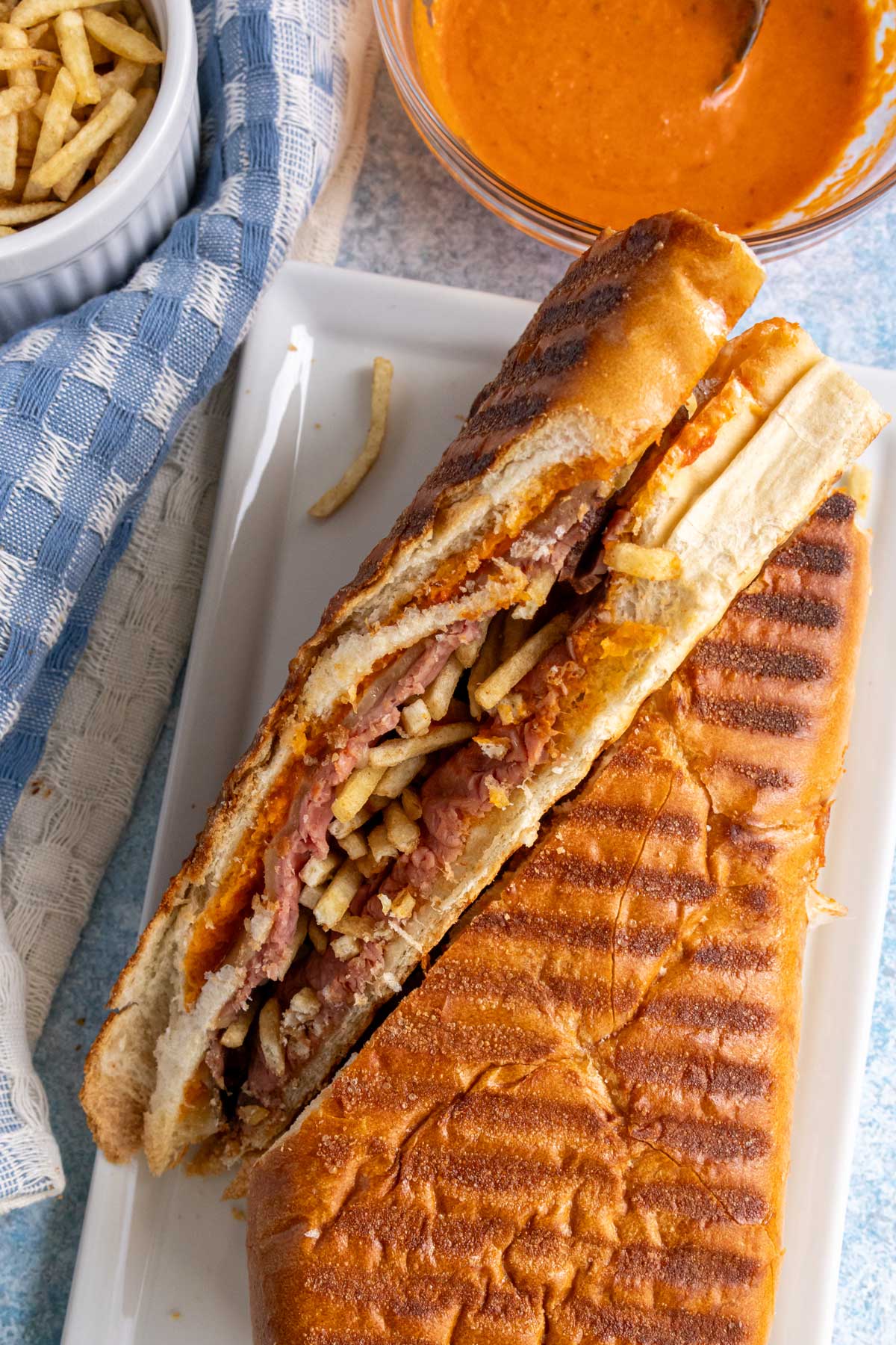 A Cuban steak sandwich cut in half diagonally on a white plate.