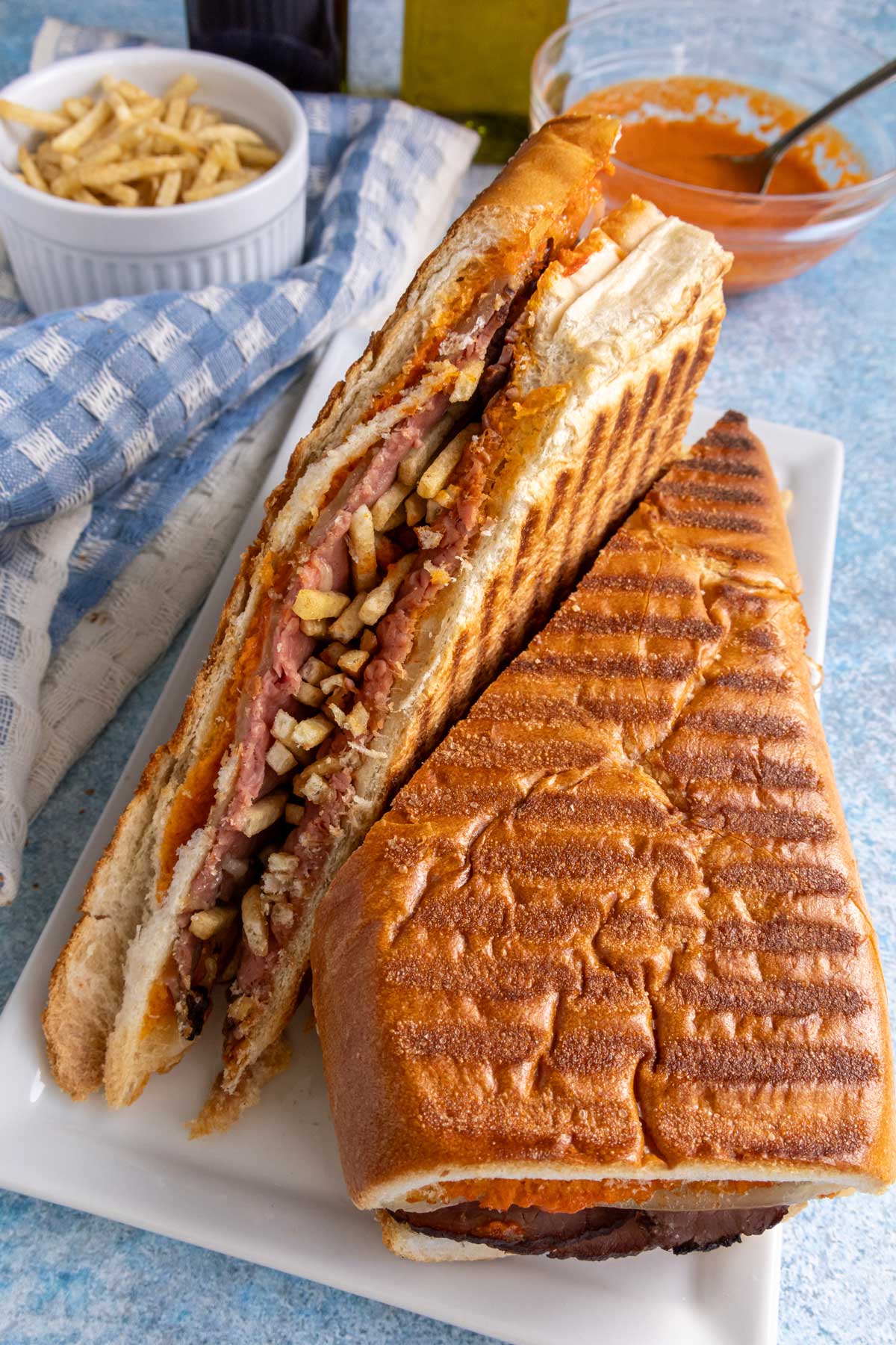 A pressed sandwich filled with roast beef, cheese, mojo rojo, and crispy potato sticks.