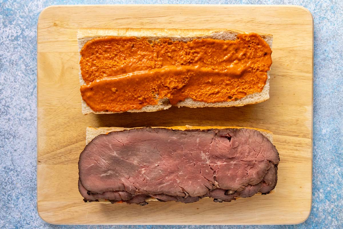 Two halves of French bread spread with mojo rojo and roast beef on one half.