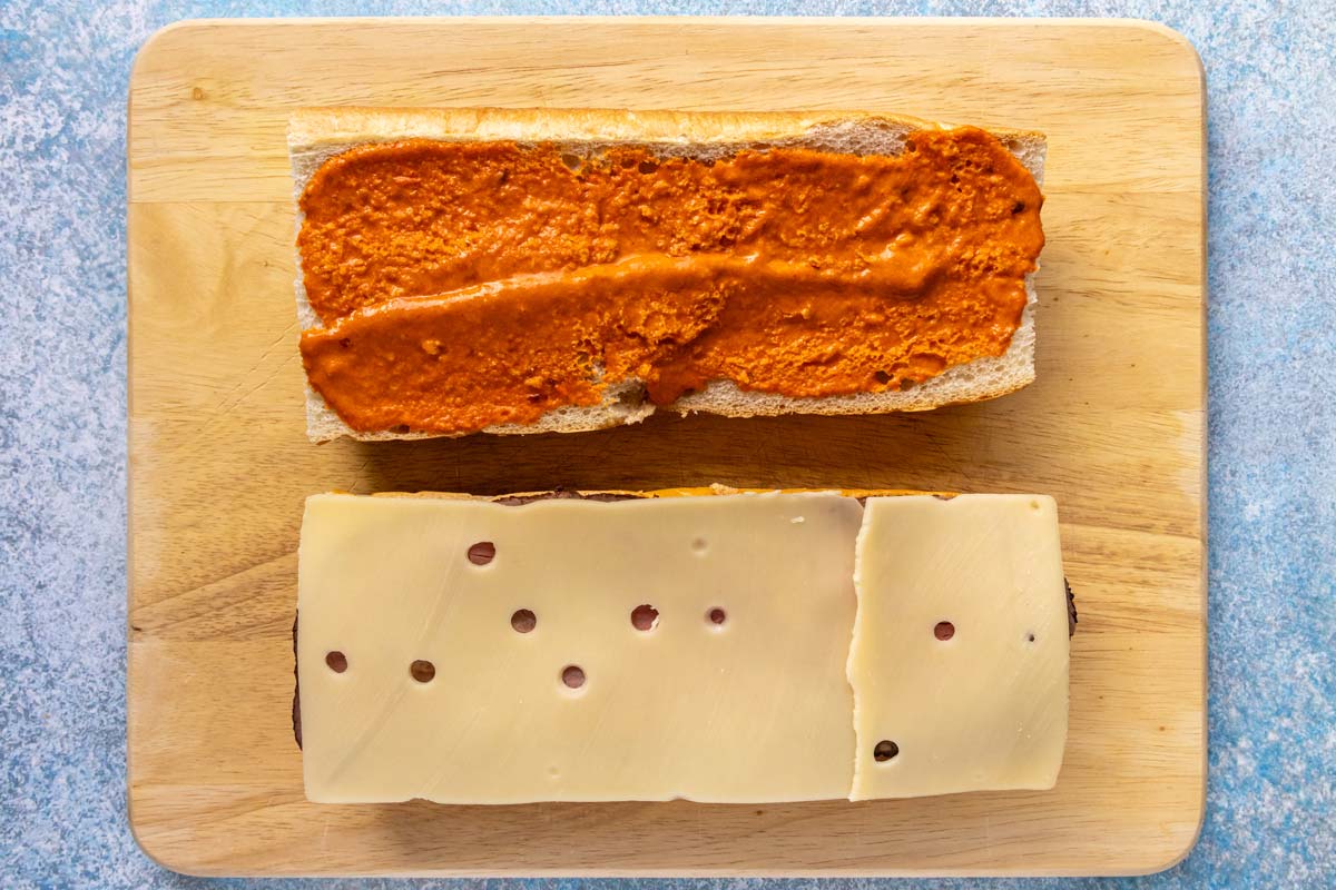 Two halves of French bread spread with mojo rojo with roast beef and Swiss cheese on one half.