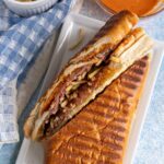 A pan con bistec sandwich inspired by Sanguich de Miami, cut in half on a white plate.