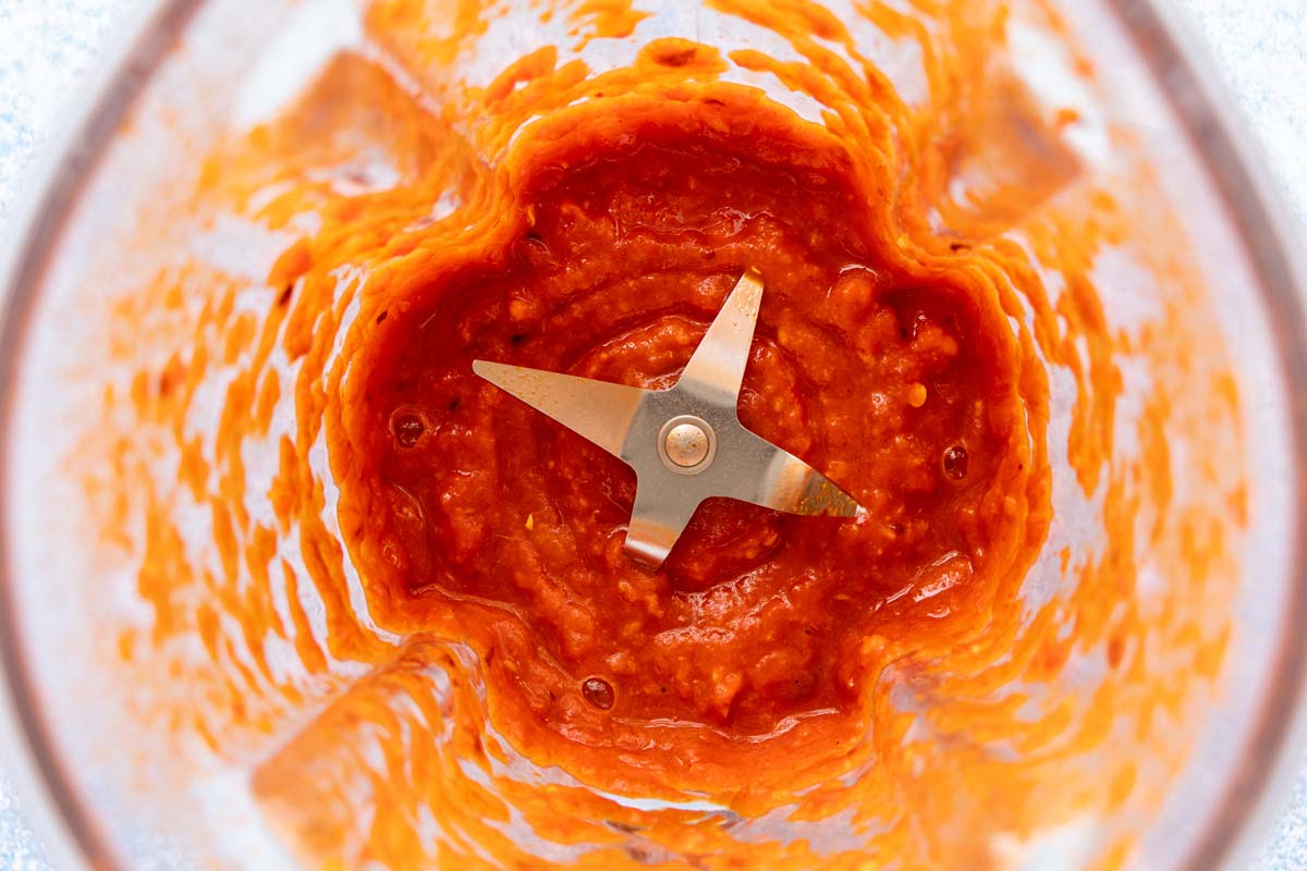 A thick red mixture in the jar of a blender.