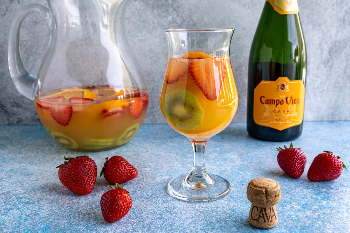 Cava sangria served in a hurricane-style glass with a pitcher and a bottle of cava in the background.