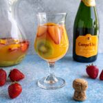 Cava sangria served in a hurricane-style glass with a pitcher and a bottle of cava in the background.