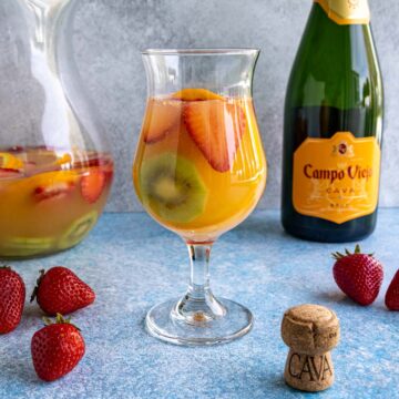 Cava sangria served in a hurricane-style glass with a pitcher and a bottle of cava in the background.