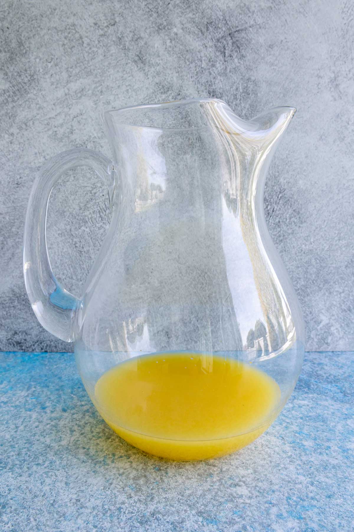 A glass pitcher with an orange juice mixture in the bottom.