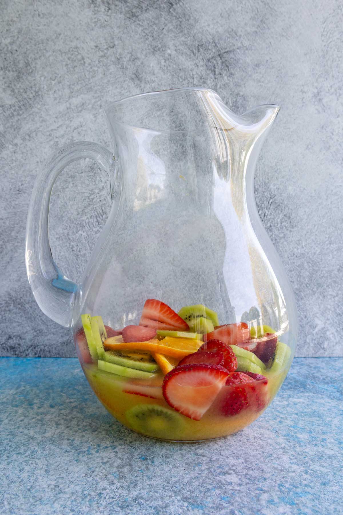 A glass pitcher with an orange juice mixture and sliced fruit in the bottom.