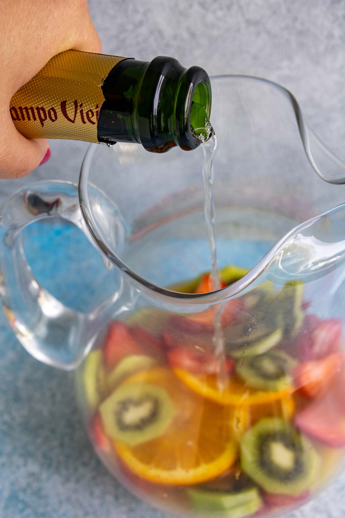 Pouring cava into a glass pitcher containing sliced fruit.