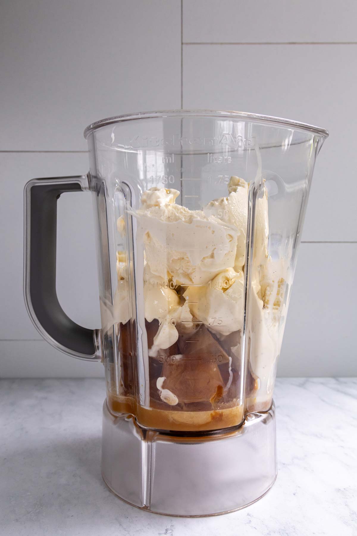 Coffee ice cubes, vanilla ice cream, and peanut butter whiskey in a blender jar before blending.
