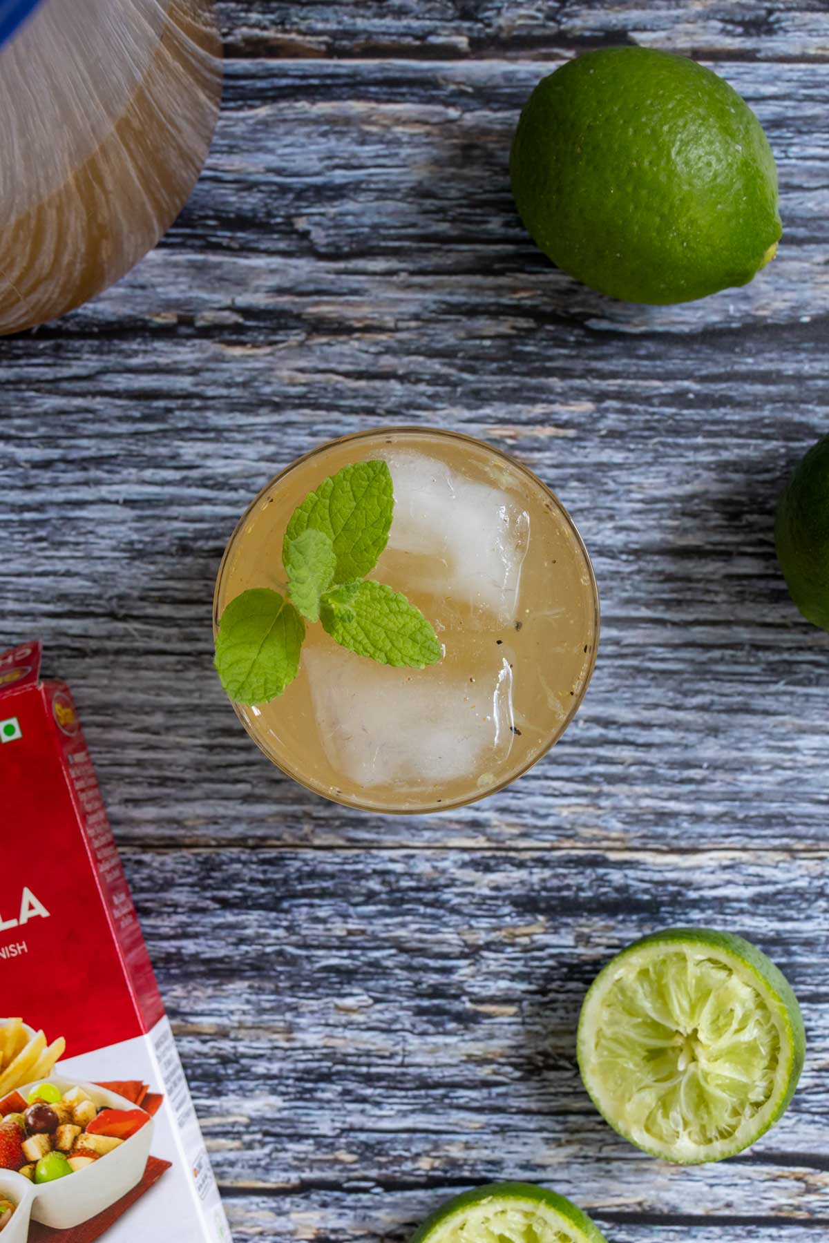 A glass of shikanji Indian lemonade on a grey wooden background with limes around it.