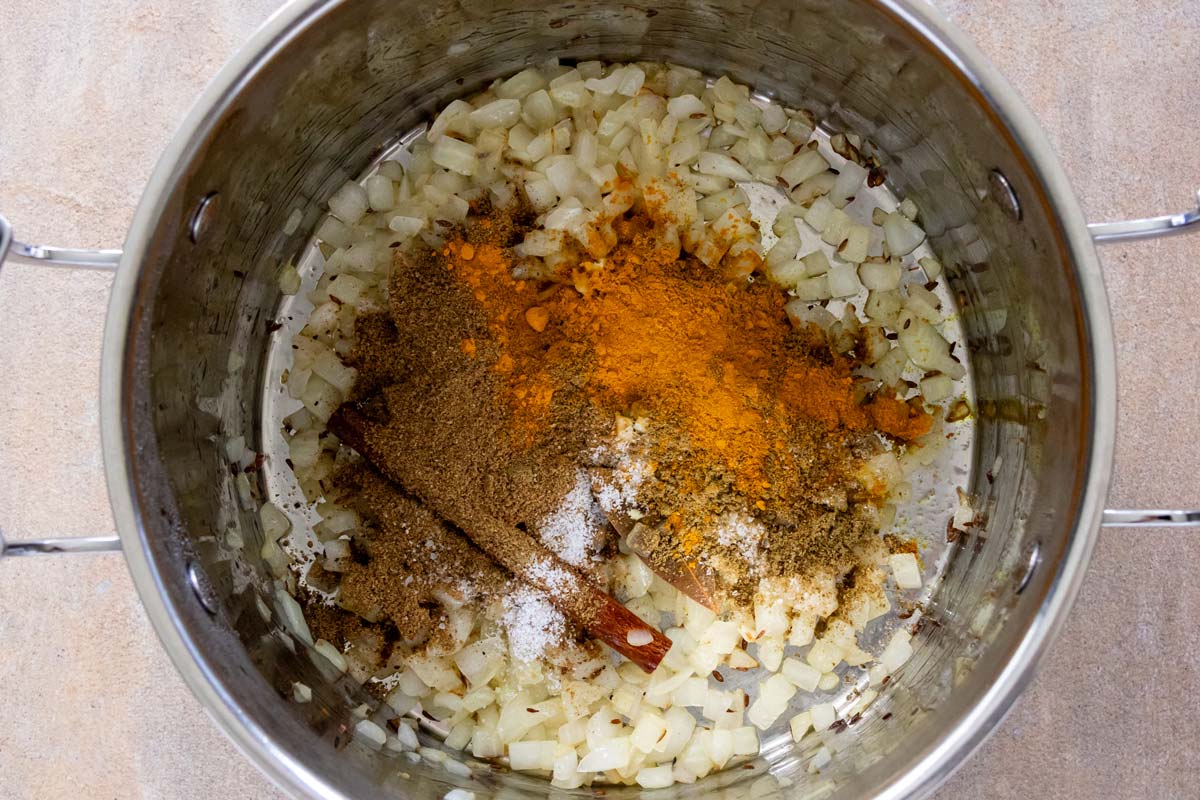 Curry seasonings added to a pot of sauteed onion.