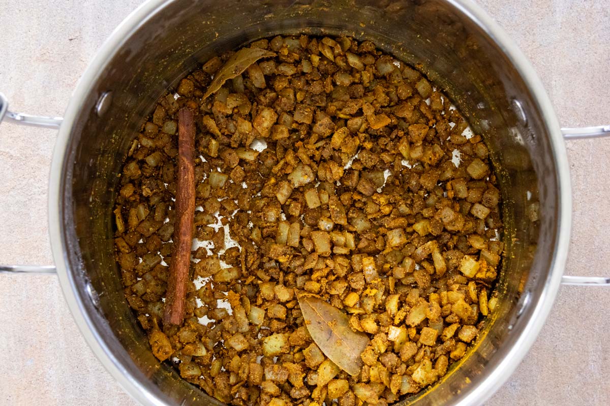 A mixture of sauteed chopped onion with curry seasonings in a pot.