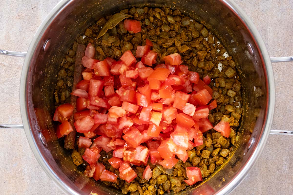 Diced tomato added to a pot of curry.