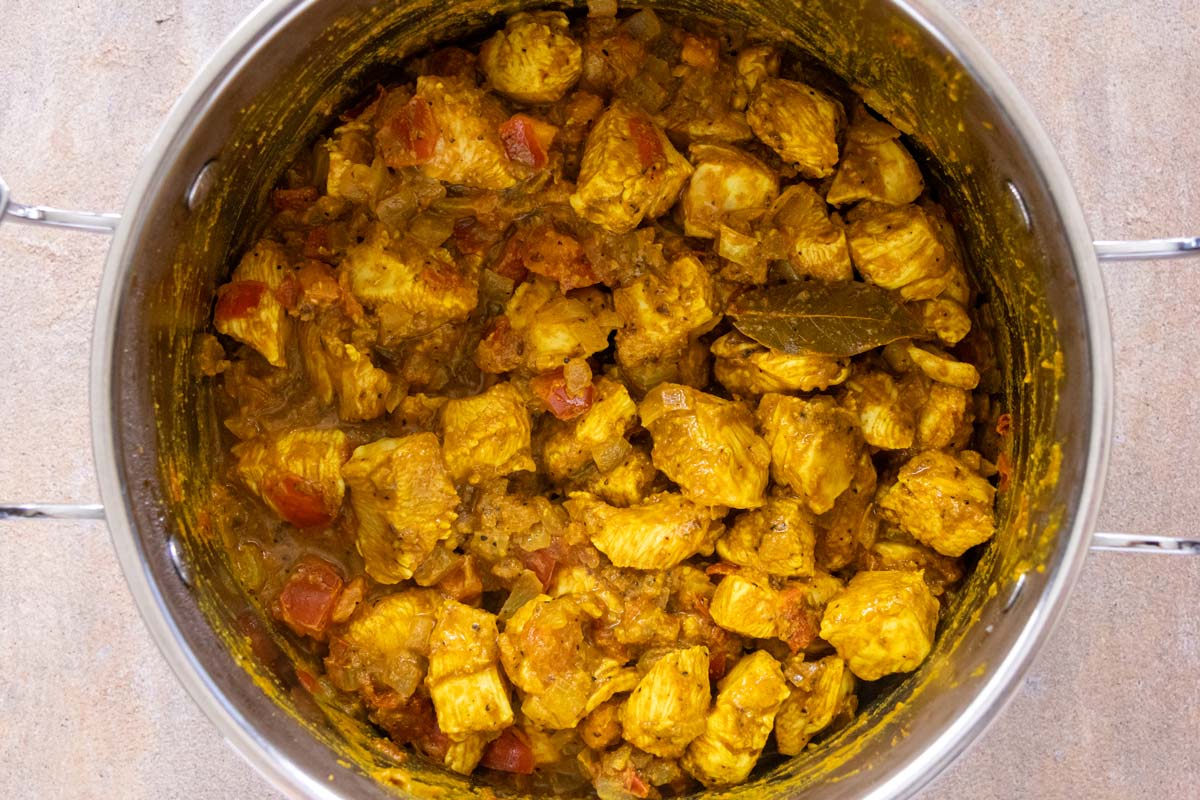 Cubed chicken combined with a curry mixture in a metal pot.