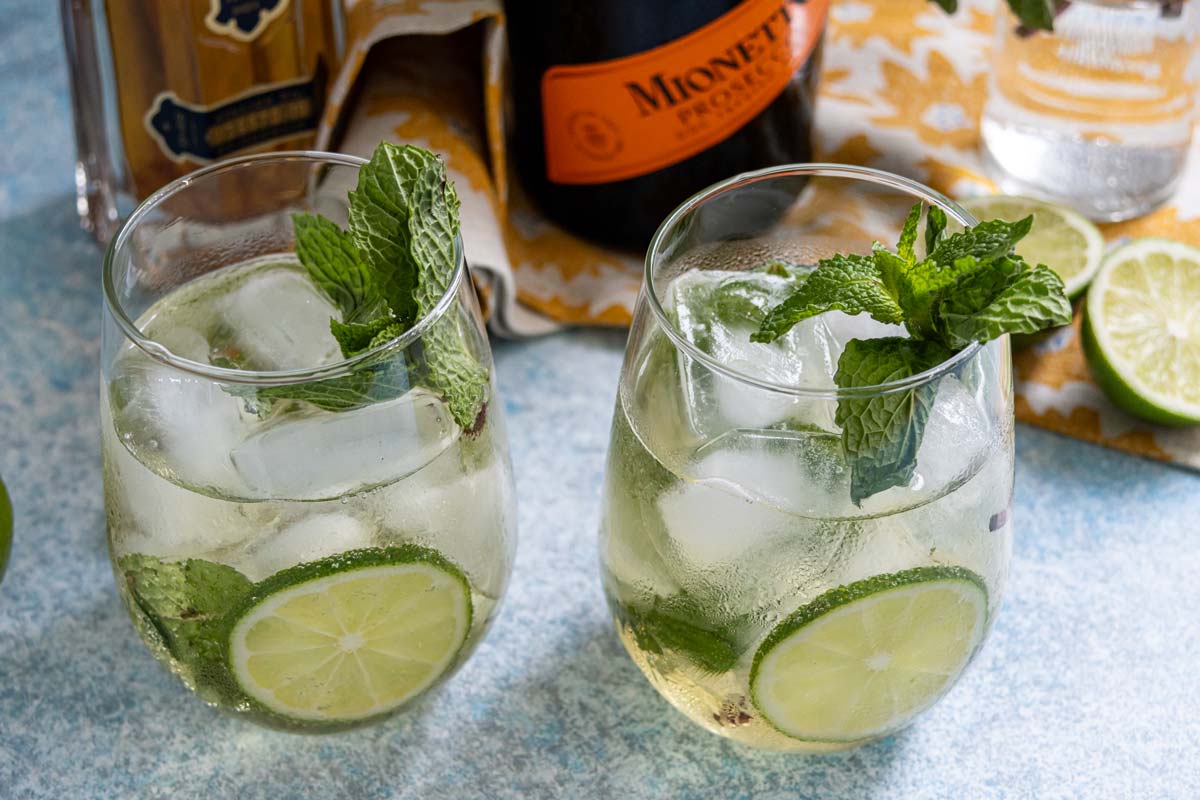 Two Hugo Spritz cocktails garnished with lime slices and sprigs of fresh mint.