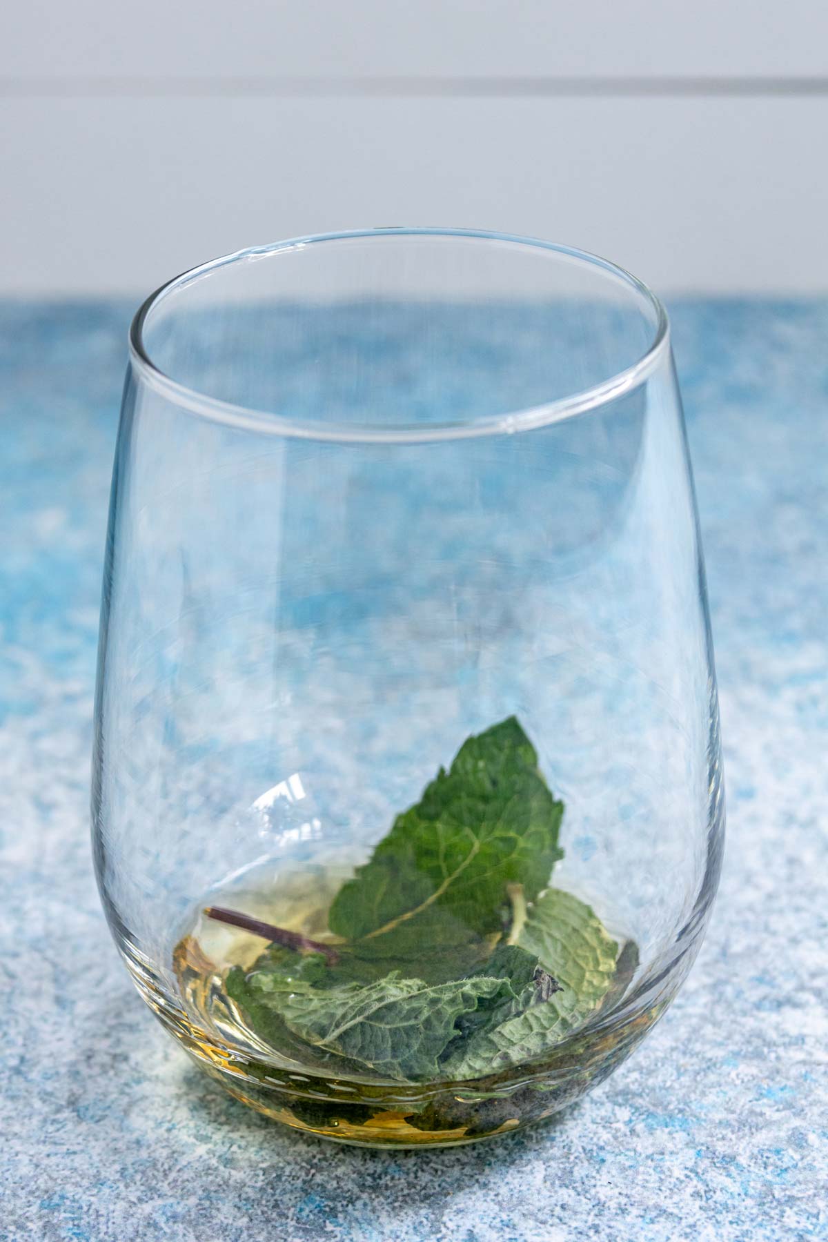 Fresh mint leaves and St-Germain liqueur in a stemless wine glass.