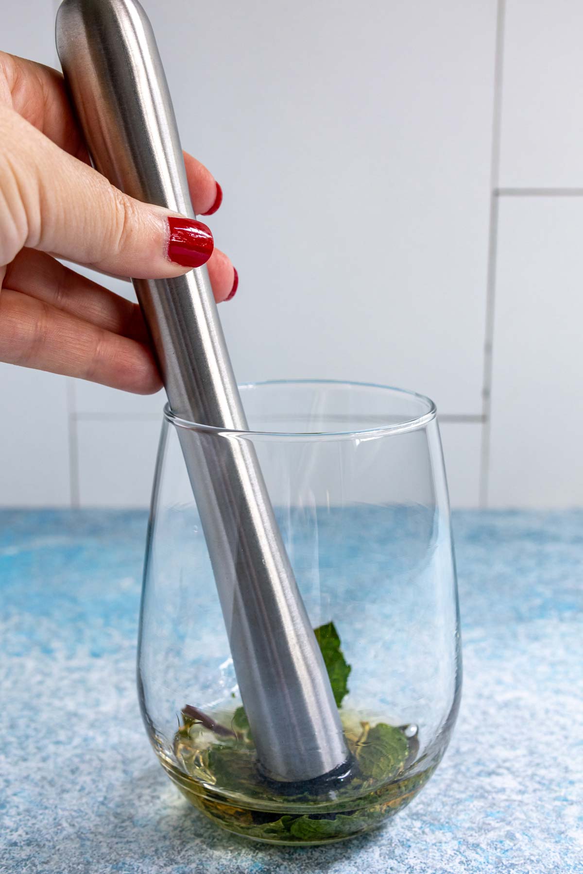 Muddling fresh mint leaves and St-Germain elderflower liqueur in a stemless wine glass.