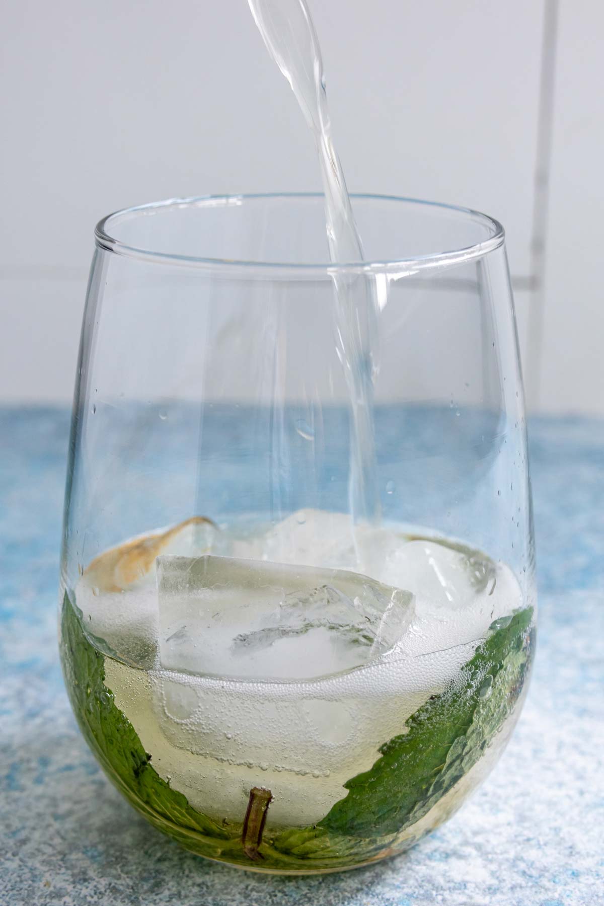Pouring prosecco into a stemless wine glass with muddled fresh mint and ice cubes.