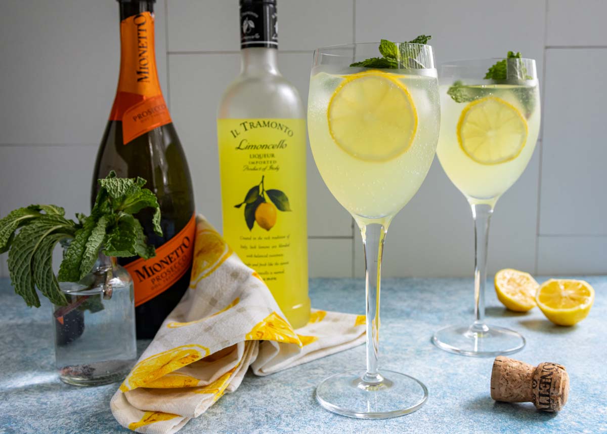 Two glasses of Limoncello Spritz surrounded by the ingredients used to make them.