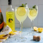 Two glasses of Limoncello Spritz surrounded by the ingredients used to make them.
